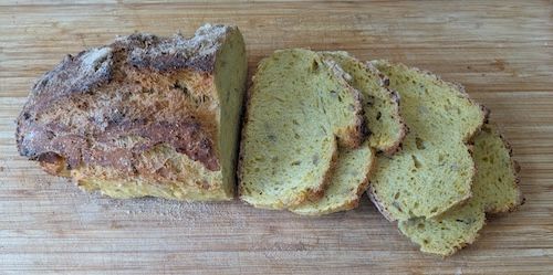 4 tranches de pain au maïs à côté du reste du pain au maïs non tranché, sur la planche à découper en bois