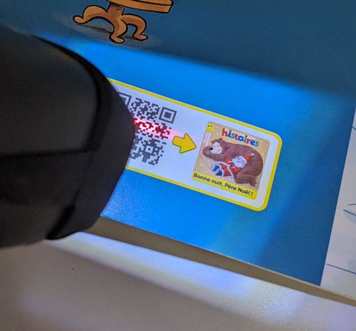Le lecteur en train de scanner un QR code sur une revue pour enfants pour écouter une belle histoire.