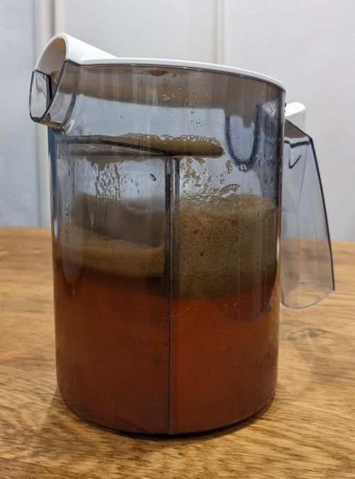 Pichet à moitié plein de jus de pomme avec de la mousse