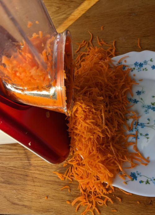Carottes râpées tombant de l’appareil dans l’assiette, avec quelques-unes à côté