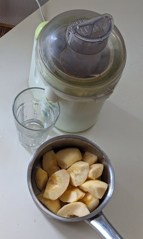 Trois pommes coupées en quartiers dans une casserole, à côté de la centrifugeuse et d’un verre vide