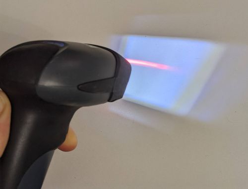 Le lecteur en fonctionnement avec le laser rouge et l’éclairage LED qui projette un trapèze de lumière blanche bleutée.